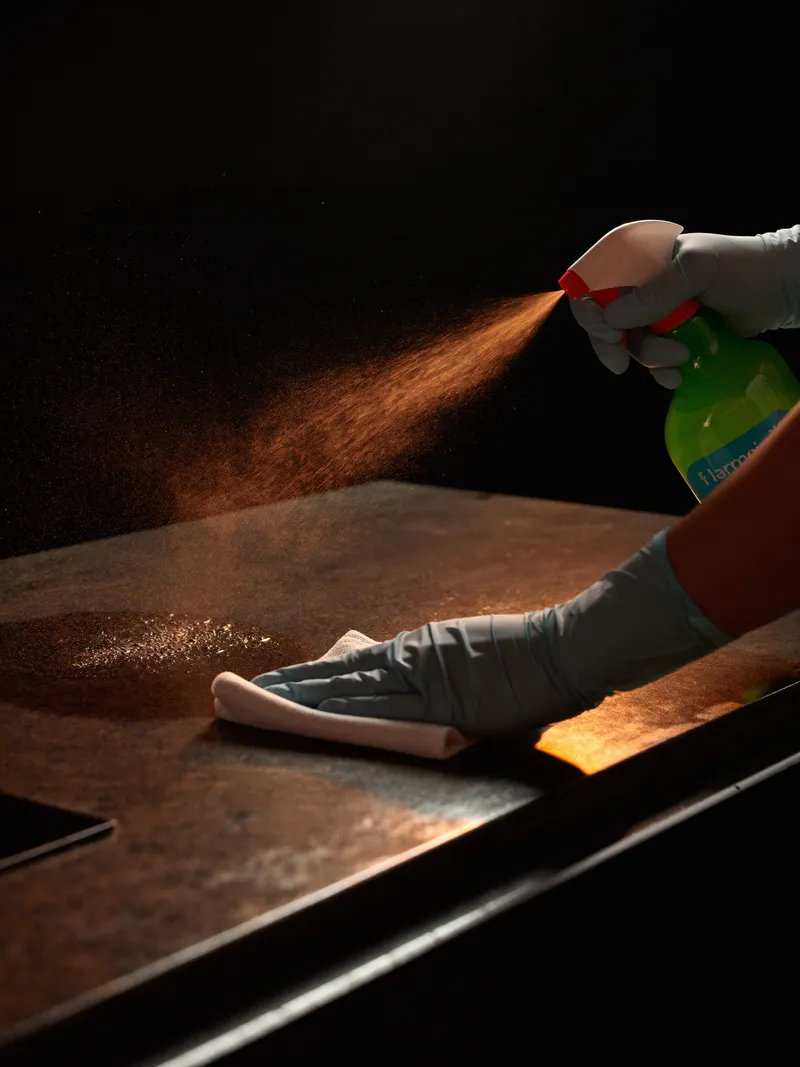 Gloved hands polishing a dark stone benchtop with a microfibre cloth, lit by a single orange light